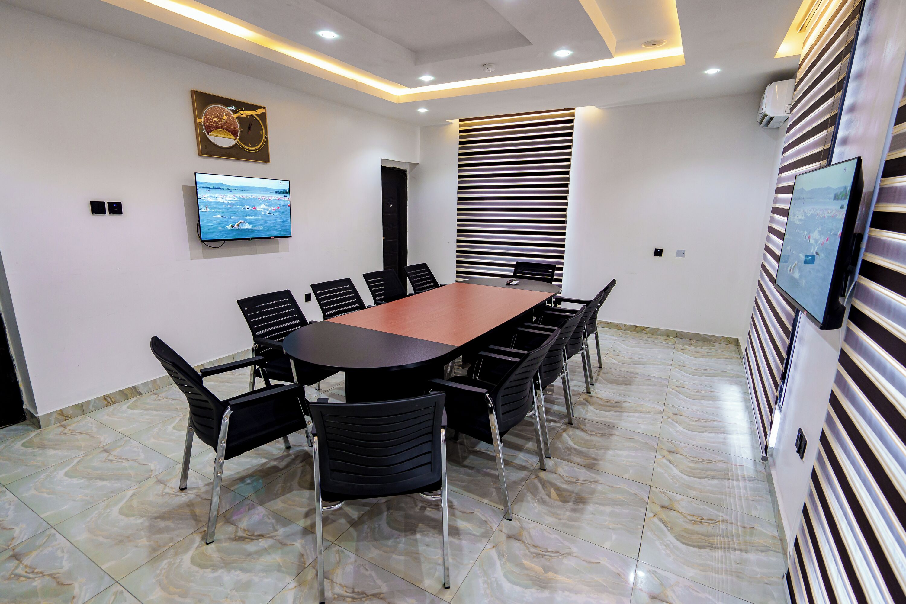 A conference room with a long table, black chairs, a mounted TV, and a striped wall panel.
