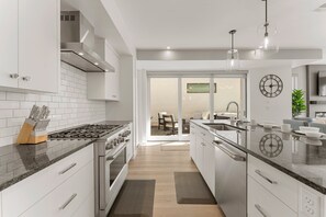A modern kitchen with white cabinets, stainless steel appliances, and a marble countertop. - Olympic Escapes Gold- Desert Color Lagoon + Beaches (St. George)