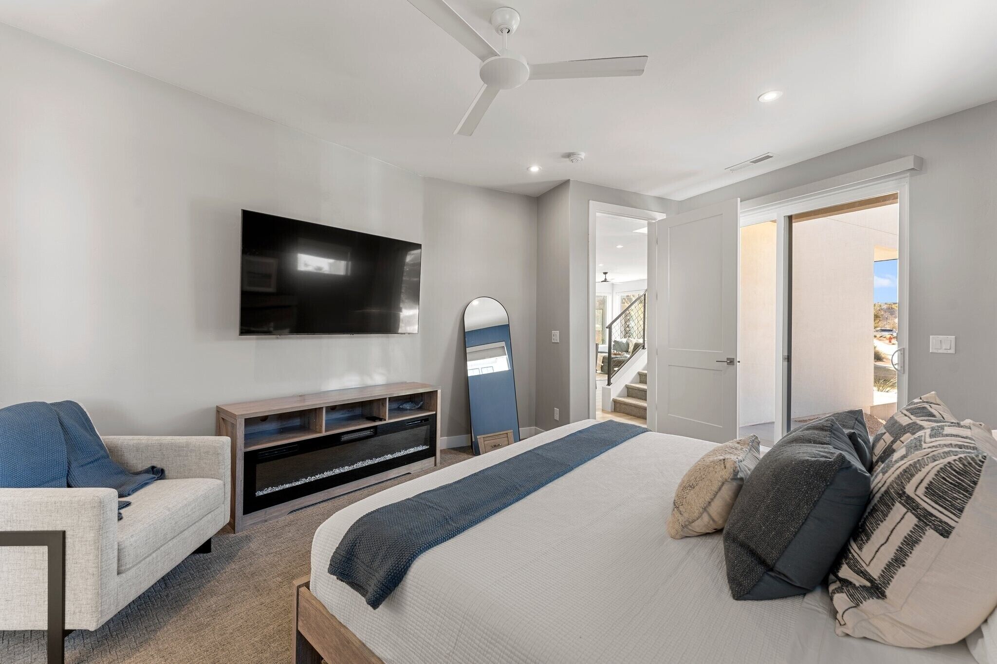 A modern bedroom with a large bed, a TV, a ceiling fan, and a door leading to a balcony.