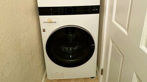 Un appareil compact, comprenant une machine à laver et un sèche-linge, conçu pour être fixé au mur, doté d’un panneau de commande et d’une poignée de porte visible.