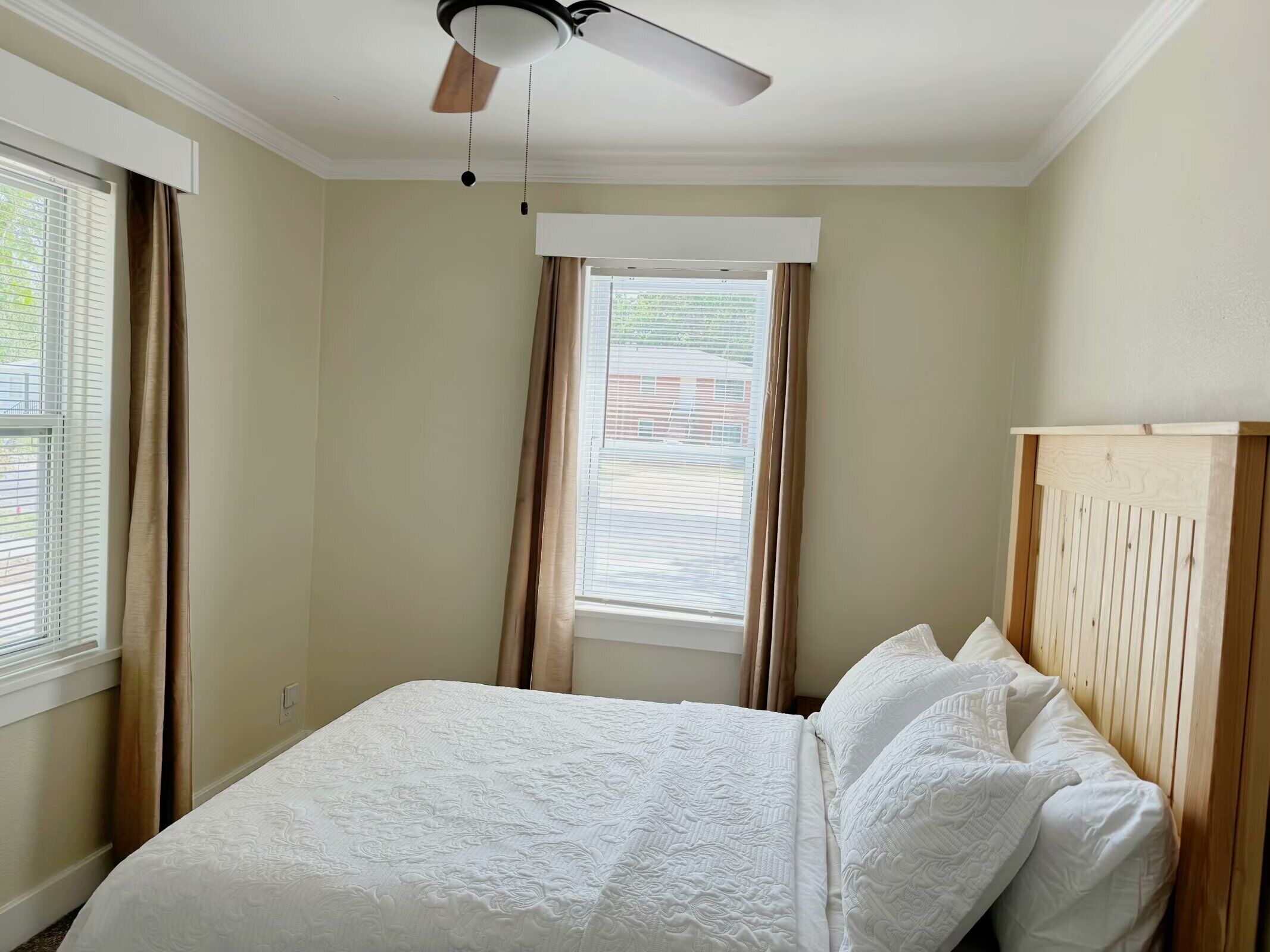 Une chambre à coucher avec un lit, un ventilateur de plafond et une fenêtre avec des rideaux.