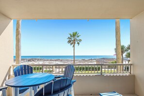 Ein Balkon mit Tisch und Stühlen, Blick auf einen Strand mit Palmen und einem Holzzaun.