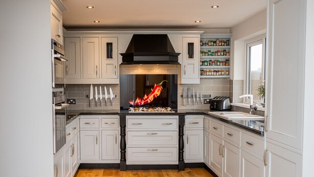 A modern kitchen with white cabinetry, a central black range hood, and a visible flame.