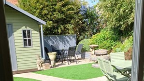 A view through a glass door into a backyard with artificial grass, a patio table, chairs, and a small shed.