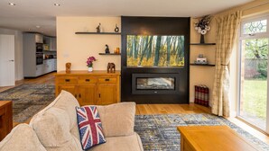 A modern living room with a fireplace, a sofa with a Union Jack pillow, and a view of a garden through large windows.
