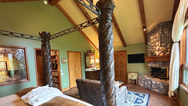 A bedroom with a four-poster bed, a stone fireplace, and a large mirror. - Forget Me Not Suite at RiverSong Inn in Estes Park - Riverside in Rocky Mountain National Park (Estes Park)