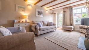 A cozy living room with a sofa, a chair, a small table, and a TV. - A delightful mid-terrace Victorian cottage only a short drive from the coast! (Docking)