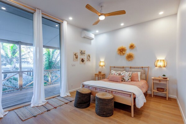 A bedroom with a bed, bedside tables, a ceiling fan, wall art, and a view of the outdoors.