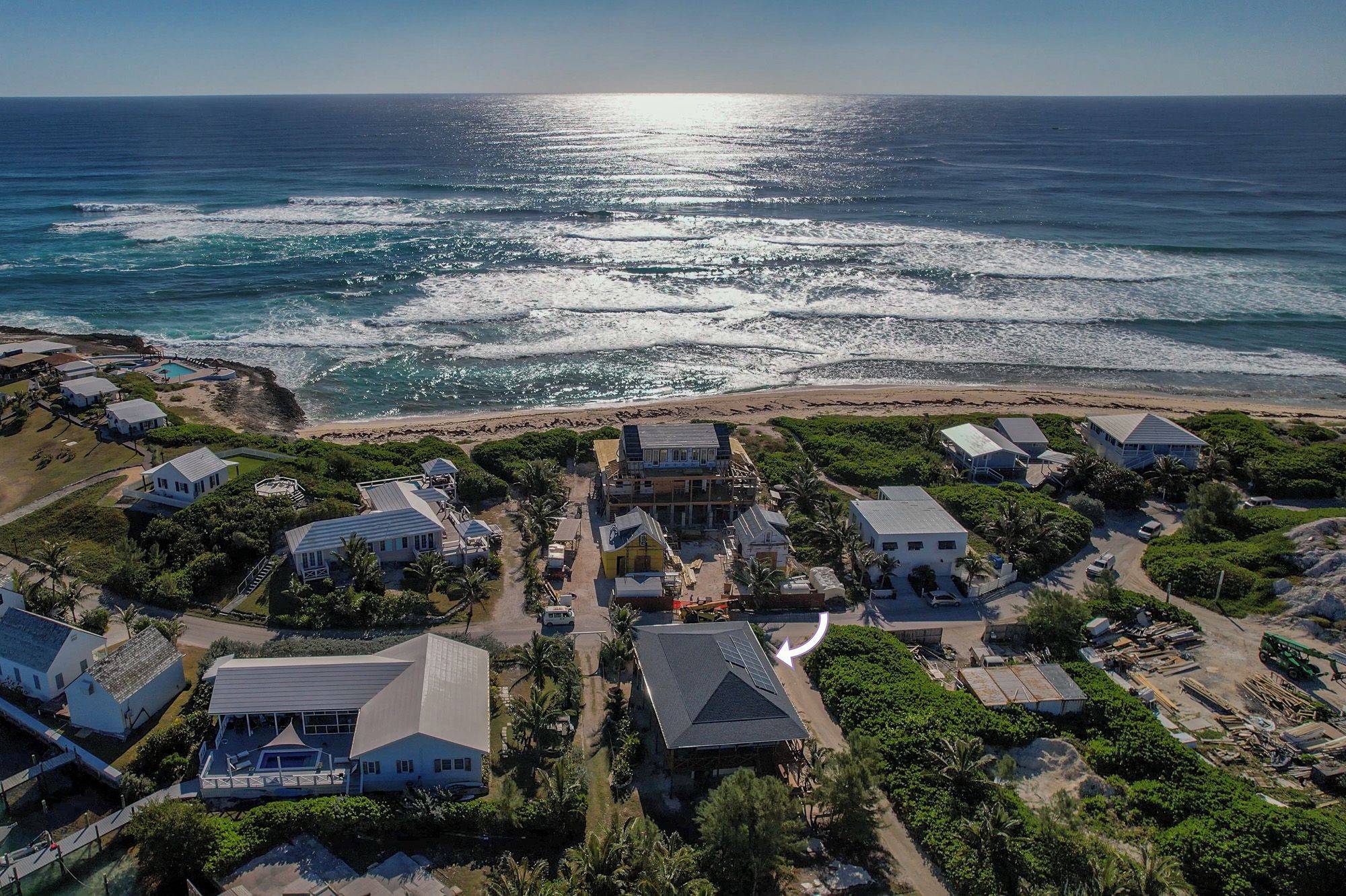 An aerial view of a coastal residential area with houses, a beach, and a clear view of the ocean.