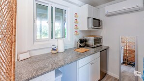 Cocina compacta con muebles blancos, encimera de granito, microondas, tostadora y ventana con vistas a zonas verdes.