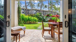Un patio con suelo de piedra, mobiliario de madera y vistas a un edificio de hotel con palmeras.