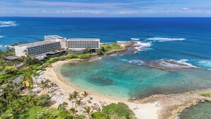 Un hotel frente al mar con varias construcciones, una playa de arena y aguas turquesas cristalinas.