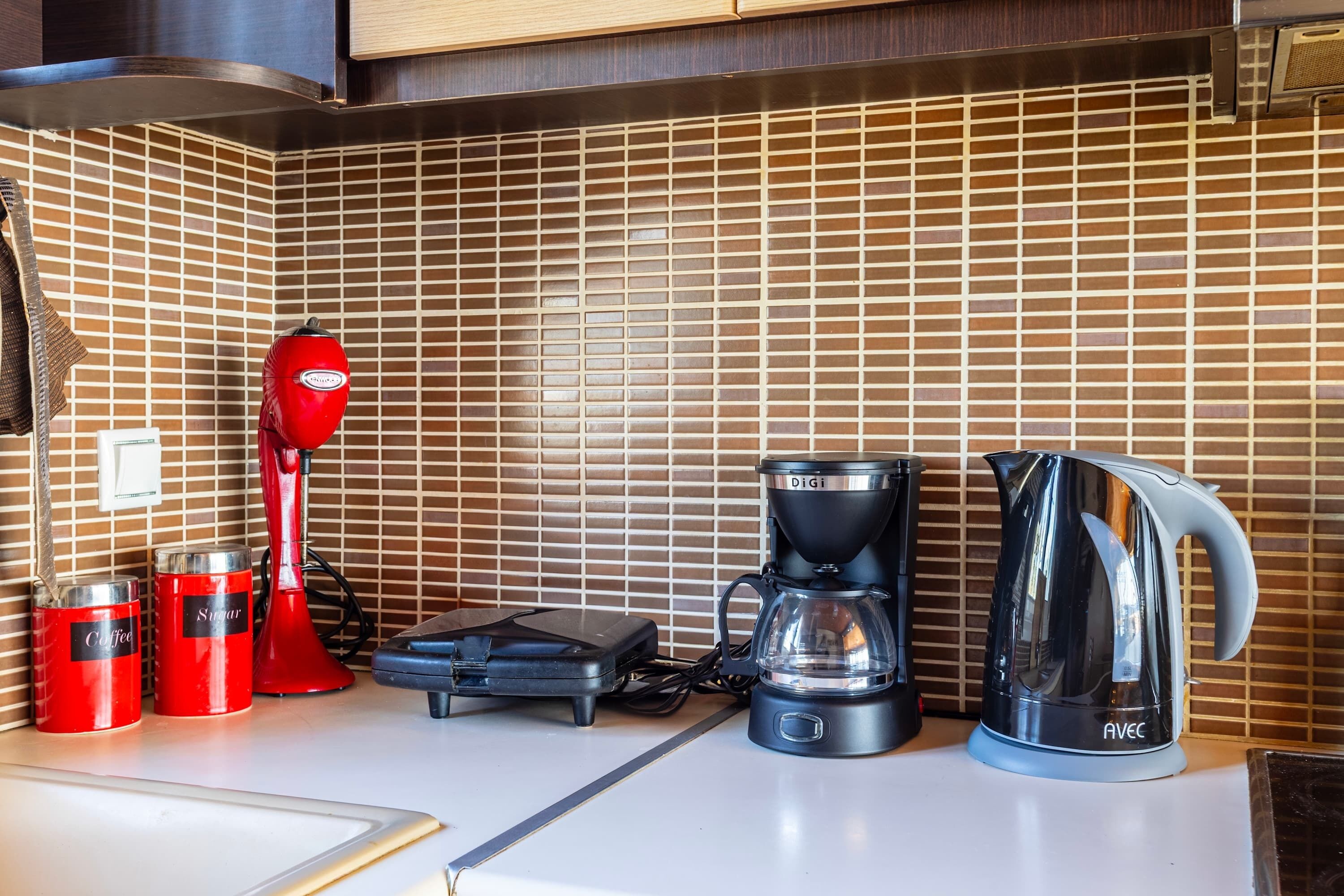 Une cuisine équipée d’une machine à café, d’un récipient à sucre et d’une bouilloire posés sur le plan de travail.