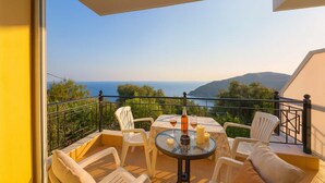 Uma varanda com mesa e cadeiras, com vista para o mar e colinas.