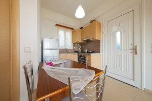 Cuina compacta amb armaris de fusta, nevera d'acer inoxidable i taula de dinar amb caires.
