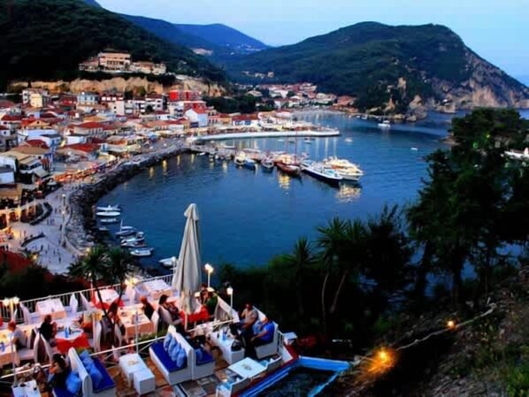 A coastal town with a marina, boats docked, and a dining area with tables and umbrellas.