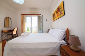 A hotel room with a bed, a desk, a chair, a lamp, and a painting on the wall.