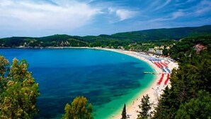 Une plage côtière aux eaux turquoise et limpides, bordée d’un rivage sablonneux, avec, en arrière-plan, de luxuriantes collines verdoyantes.
