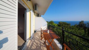 Un balcon avec une table et des chaises en bois, une porte blanche et une vue sur la mer.