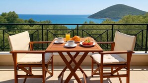 A wooden table with two chairs, a breakfast setting, and a scenic view of the sea and a hill. - Ionian View Gem - Parga Ethereal Nest (Agia Kiriaki)