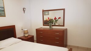 A hotel room with a bed, a wooden dresser, a nightstand with a lamp, a mirror, and a wall-mounted picture.