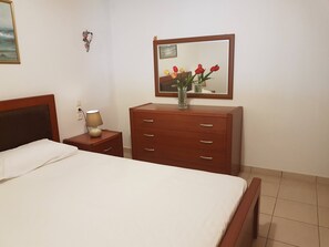 A hotel room with a bed, a wooden dresser, a nightstand with a lamp, a mirror, and a wall-mounted picture. - Ionian View Haven - Parga Panoramic Seaview (Agia Kiriaki)
