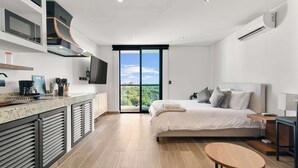 A modern bedroom with a large bed, a small bedside table, a TV mounted on the wall, and a view of the outdoors through a sliding door.