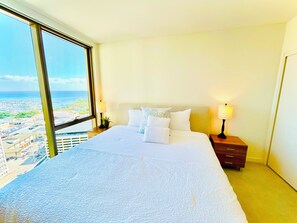 Une chambre d’hôtel avec un grand lit, deux tables de chevet et une vue sur la ville grâce à une grande fenêtre.