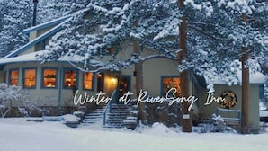 A cozy lodge with a snow-covered exterior, a visible entrance, and a lit interior suggesting a warm interior. - Chiming Bells Suite at RiverSong Inn in Estes Park - Riverside in Rocky Mountain National Park (Estes Park)