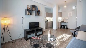 Una sala de estar moderna con televisor, mueble negro para equipo audiovisual, mesa de centro de vidrio y una lámpara de pie.