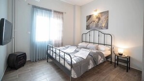 Un dormitorio con cama, una mesita de noche con lámpara, un televisor montado en la pared y una ventana con cortinas.