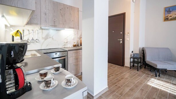 Una cocina moderna con cafetera, una mesa de comedor con tazas y una zona de estar acogedora con una silla y una mesa.