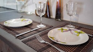 Una mesa de comedor dispuesta con dos platos, dos copas de vino y cubiertos sobre un mantel tejido.