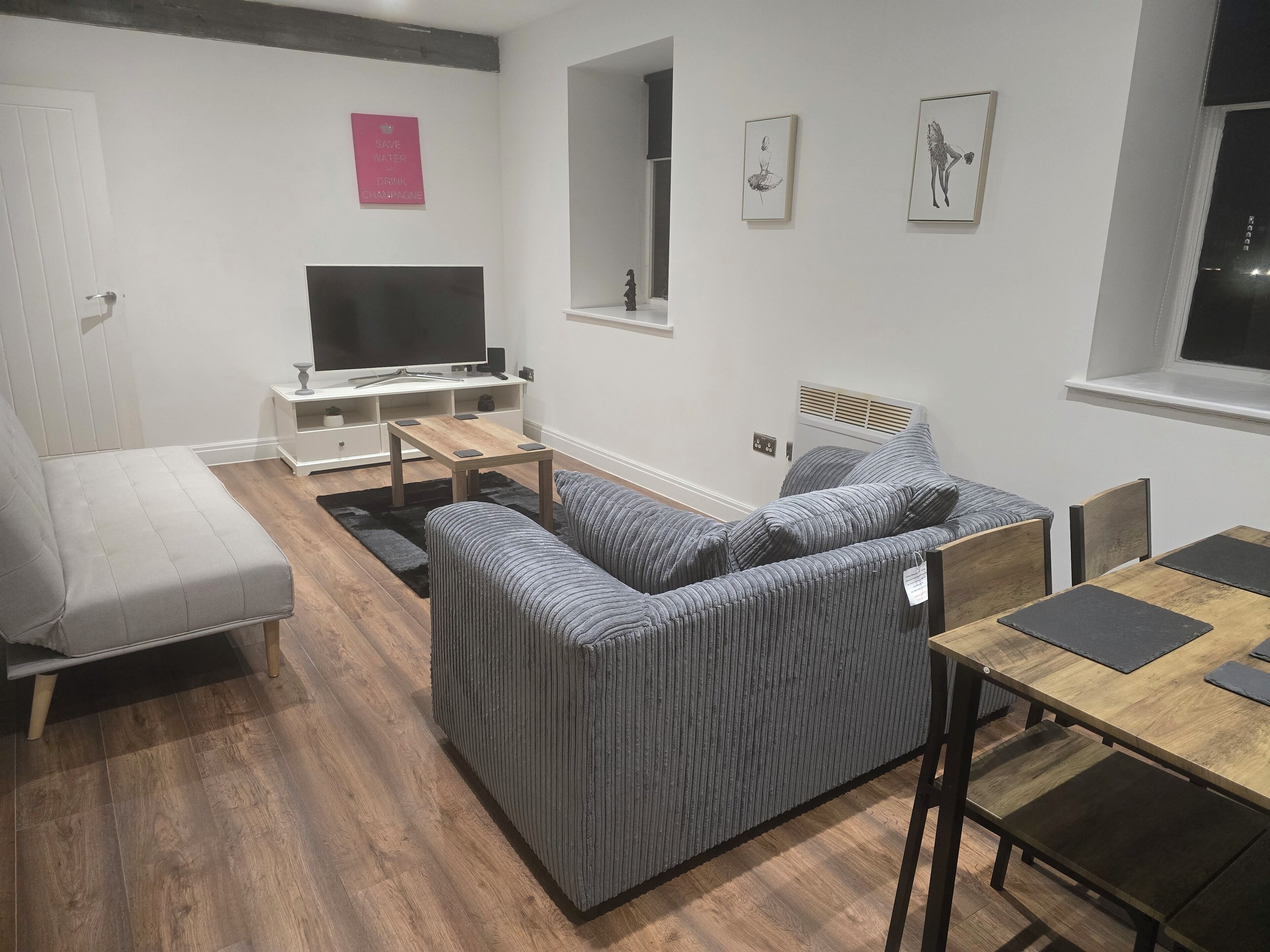 Un salon moderne avec un canapé gris, une table basse en bois, un téléviseur et des œuvres d’art accrochées aux murs.