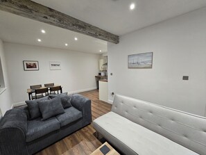 A modern living room with a grey sofa, a white bench, and a dining area with wooden chairs and a table.