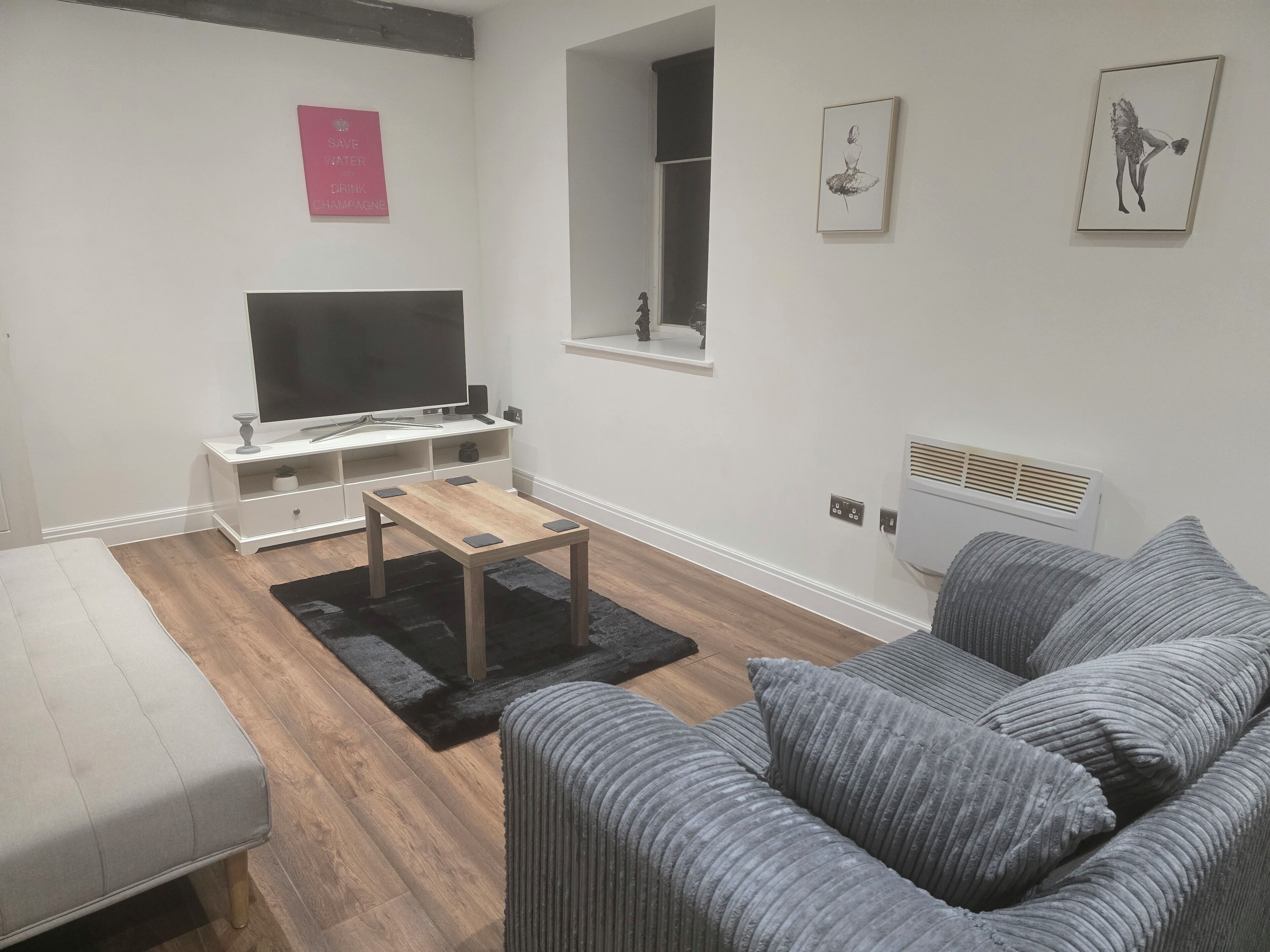 A modern living room with a flat-screen TV, a wooden coffee table, a grey sofa, and a black rug.