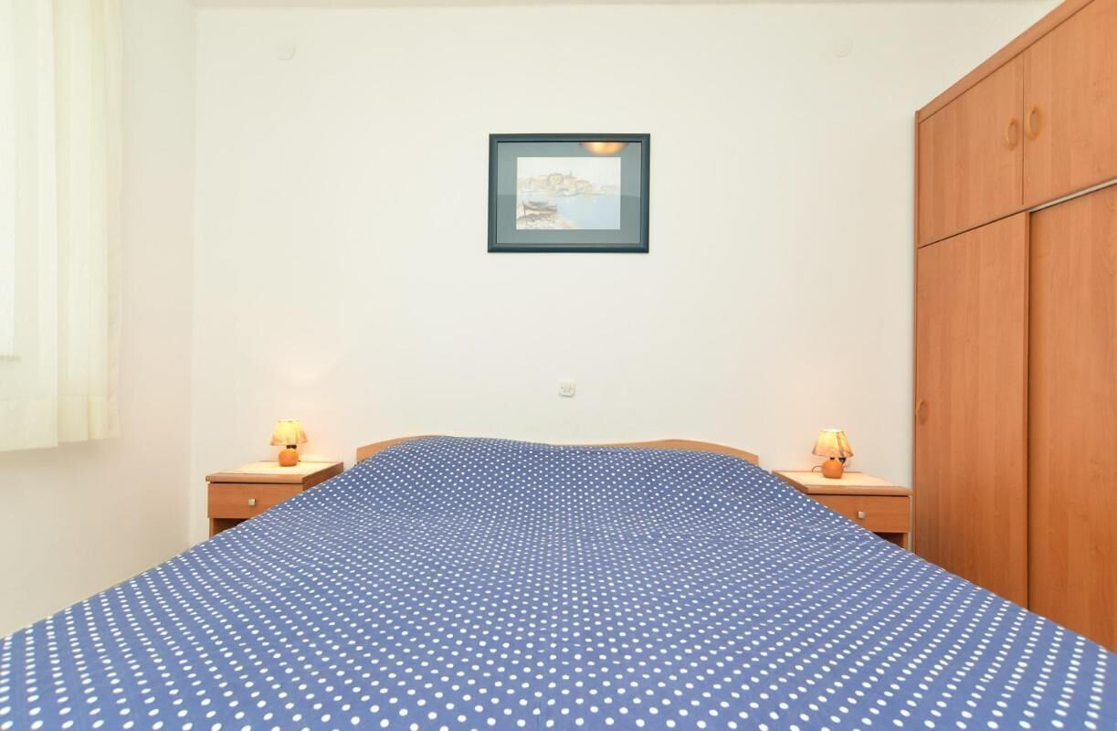 A bedroom with a bed, two bedside tables, a wooden wardrobe, and a framed picture on the wall.