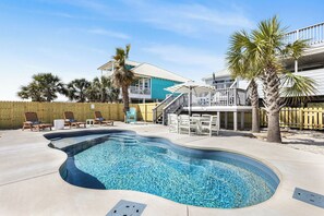 A swimming pool with a curved edge, surrounded by lounge chairs and a wooden fence. - 1 Block to Beach, Heated Private Pool, Fire Pit, Family‑Friendly, Walk to Dining (Gulf Shores)