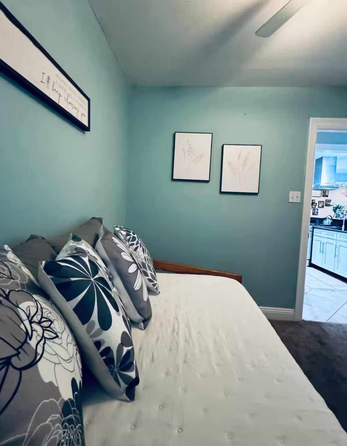 Een slaapkamer met een bed, kussens en twee kunstwerken in lijsten aan de muur.