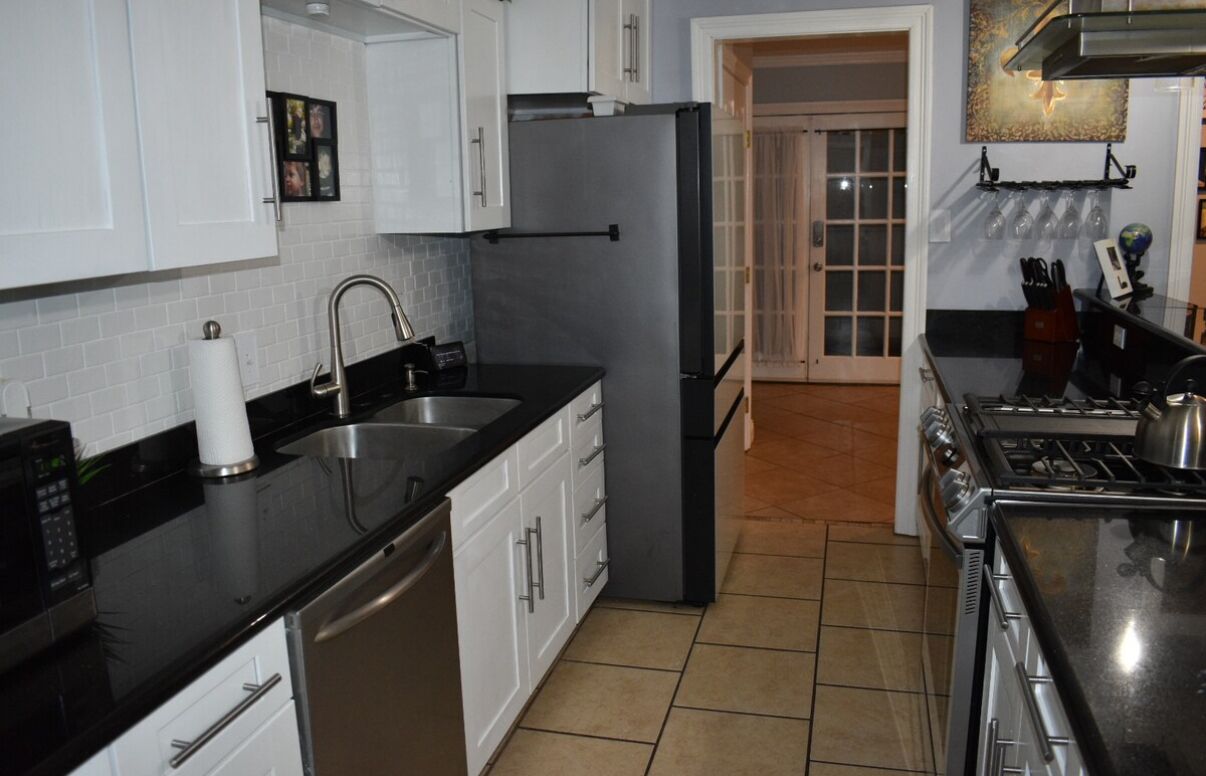 A modern kitchen with white cabinets, a black countertop, stainless steel appliances, and a tiled floor.