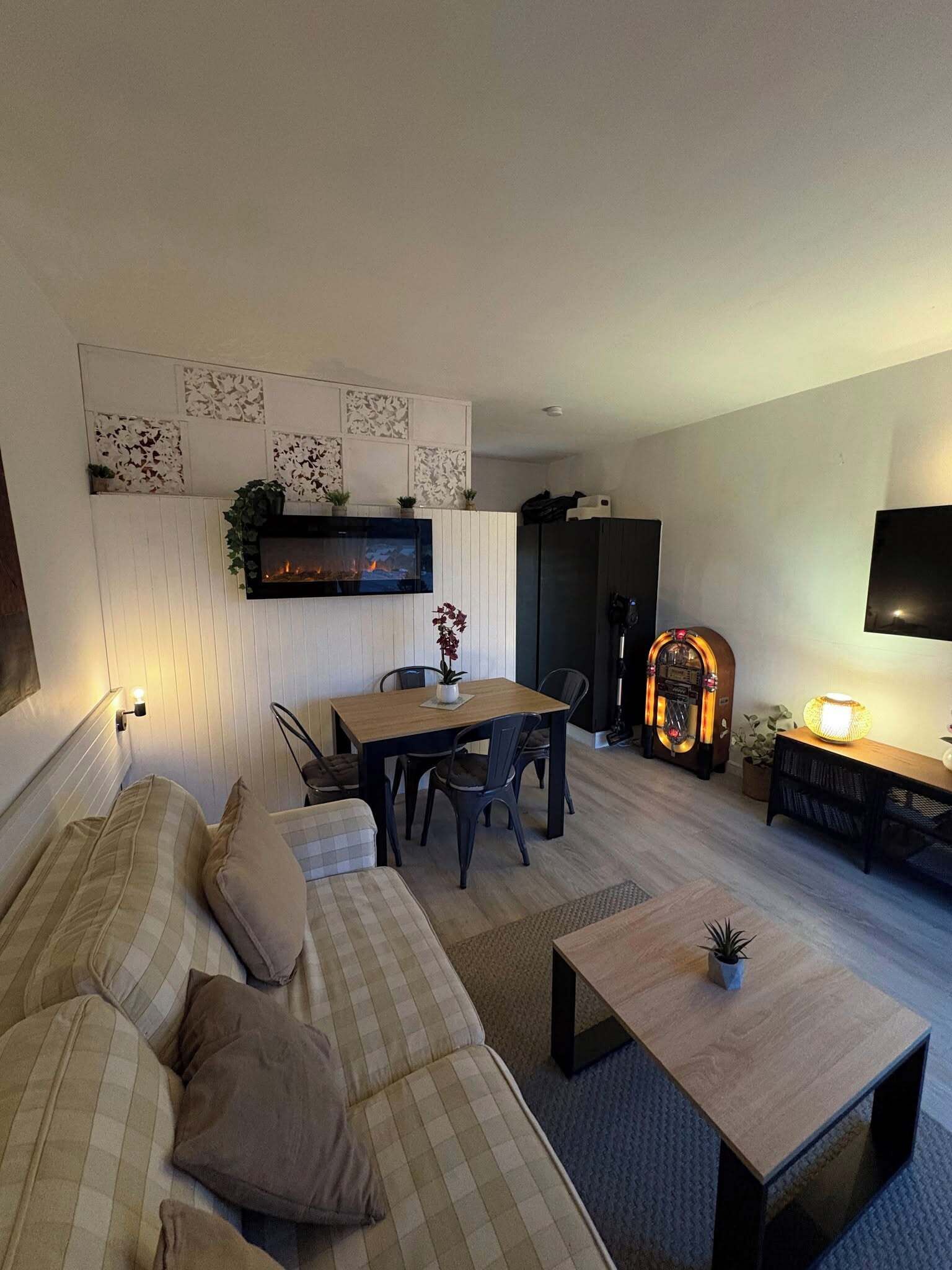 A modern living room with a sofa, dining table, chairs, a TV, a fireplace, and a jukebox.