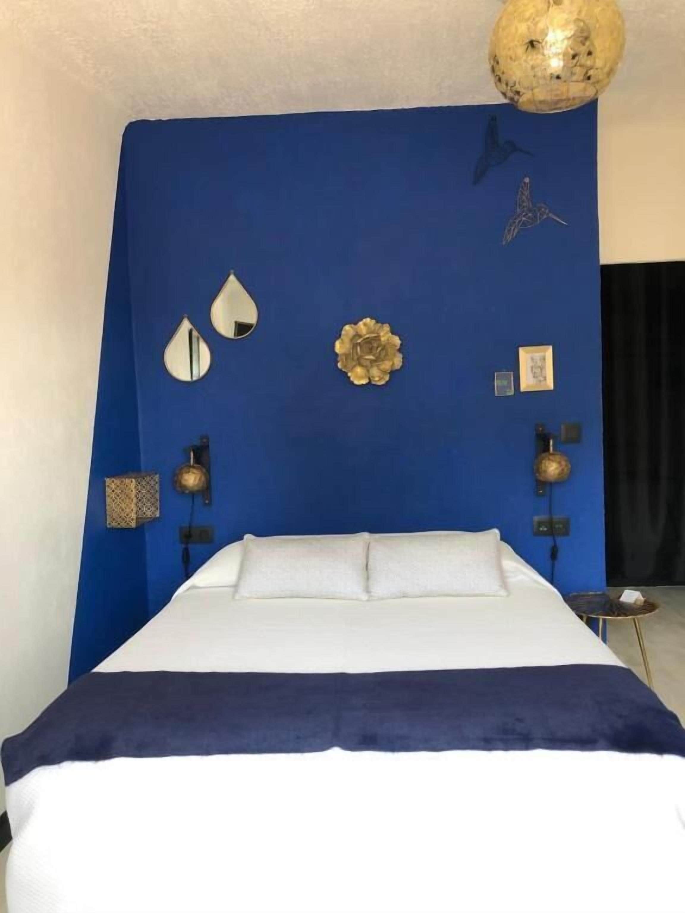 Een slaapkamer met een groot bed, een blauwe accentmuur en decoratieve wandkunst, waaronder een wereldbol en een vogel.