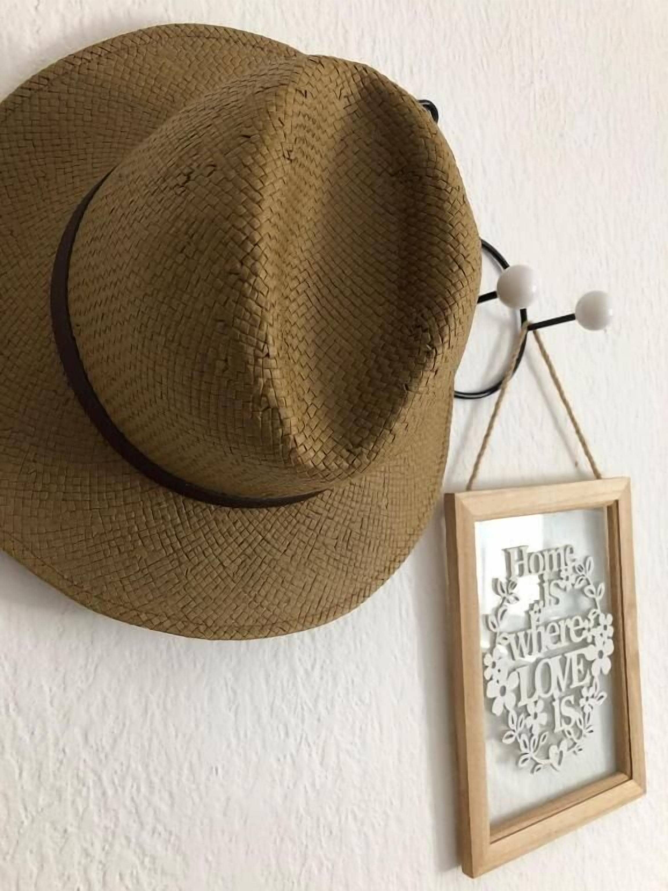 Un sombrero de paja y un cartel enmarco con el texto "Home is where love is" en una pared blanca.