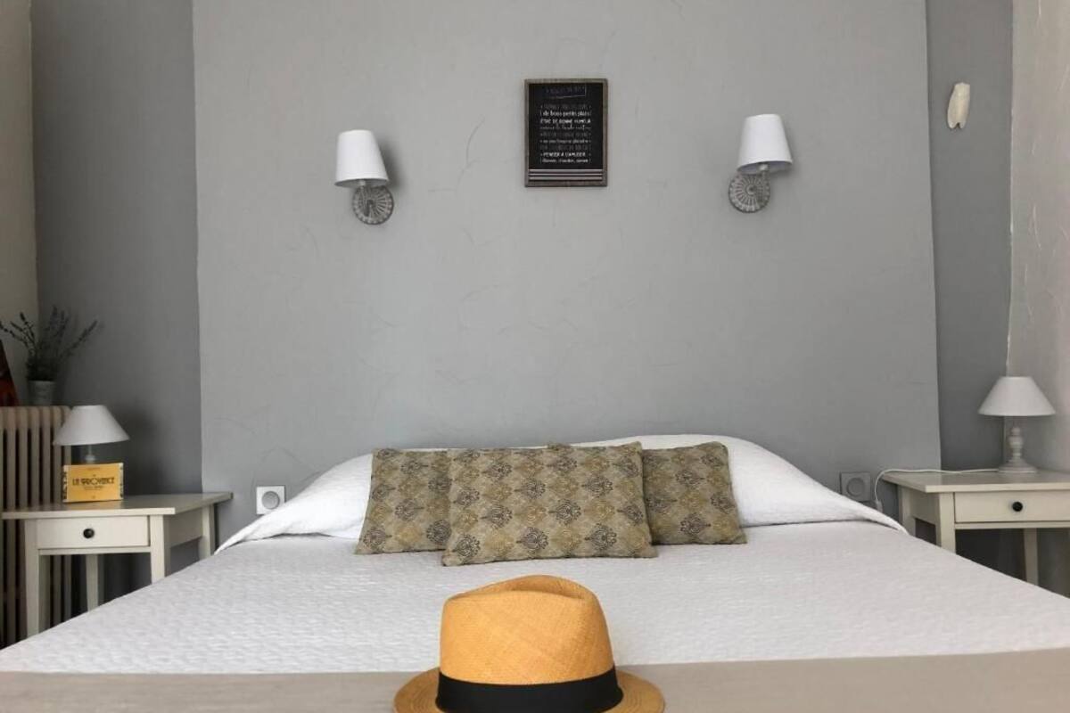 Quarto de hotel bem organizado, com cama, duas luminárias de cabeceira, relógio fixado na parede e uma mesinha com abajur.