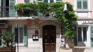 Un bâtiment rose aux volets verts, une porte en bois et un balcon orné de plantes.