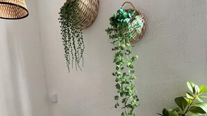 Un bureau blanc avec un ordinateur portable, deux paniers suspendus contenant des plantes vertes et un panier en osier avec une plante, le tout placé devant un mur blanc.