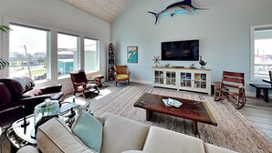A spacious living room with a large sofa, a coffee table, and a television. There are two chairs, a rug, and a cabinet with decorative items.