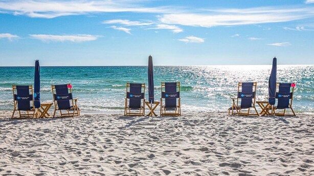 A beach with rows of wooden lounge chairs and umbrellas, arranged for sunbathing.
