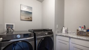 A laundry area with two Samsung washing machines, a drying rack, and a marble countertop with cleaning supplies. - Newly Built Retreat | Comfort & Ski Access (American Fork)