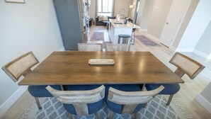 A dining area with a wooden table and blue upholstered chairs, a kitchen in the background, and a patterned rug on the floor. - Newly Built Retreat | Comfort & Ski Access (American Fork)
